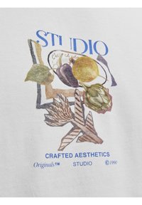 Hvid bomulds t-shirt med et farverigt grafik af frugt og grøntsager. Teksten lyder "STUDIO" i blåt over "CRAFTED AESTHETICS" og "Originals™" i blåt.