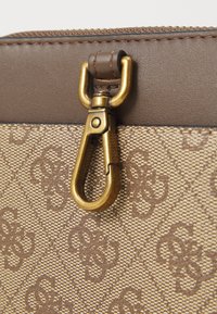 Brown leather bag corner with a gold metal clasp and a textured fabric patterned with dark brown interlocking letters.