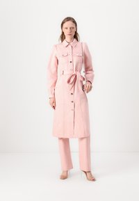 Rosa denim skjortekjole med lange ermer, knappestolpe, to brystlommer og tilhørende belte, sammen med rosa vide bukser og hæler.