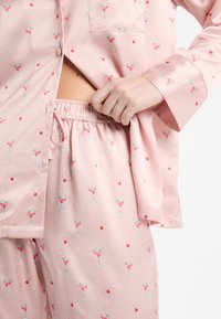 Różowy pasiasty komplet piżamowy z małymi wzorami kieliszków koktajlowych i wiśni. Miękki materiał, swobodny krój z elastyczną talią i boczną kieszenią.