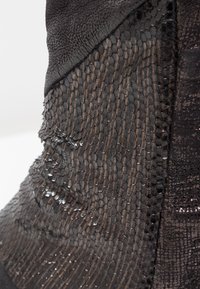 Black ankle boot featuring textured leather with a scale-like pattern, shiny accents, and a smooth surface, highlighting varying finishes.