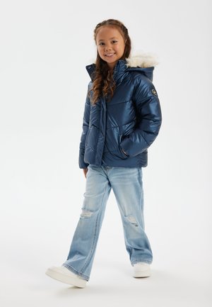 Marinblå pufferjacka med faux päls på huvan, sömdesign, dragkedja fram och två sidofickor, kombinerad med ljusblå rivna jeans och vita skor.