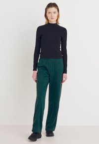 Svart langermet skjorte kombinert med teal velourbukser med et subtilt mønster, komplementert av svarte sko. Enkel, tettsittende design.