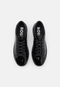 Zapatillas de charol negro con cordones planos, puntera redondeada y plantillas acolchadas. Presentan un logo en la plantilla y un elegante detalle en los laterales.