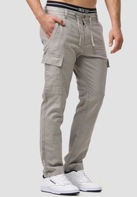 Szare spodnie cargo z troczkiem i zapięciem na guzik, z kieszeniami bocznymi i przeszywanym pasem. Połączone z białymi trampkami.