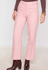 Pantalons ajustés rose clair avec une jambe droite, tissu texturé, poches avant et passants de ceinture, associés à des bottes de cheville sombres.