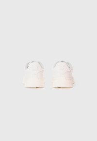 Un paio di sneakers bianche con il logo "HUGO" sul tallone, esposte da dietro su uno sfondo grigio chiaro e uniforme.