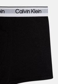 Čierne bavlnené boxerkové šortky so širším elastickým pásom v bielej a šedej farbe s logom "Calvin Klein", hladká textúra a obtiahnutý strih.