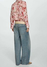 Blusa cropped floreale rosa con maniche lunghe, abbinata a jeans denim larghi di colore azzurro. La vista posteriore mostra una vita elastica e tasche posteriori discrete.