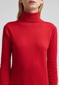 Roter Rollkragenpullover aus weichem Strickstoff, mit langen Ärmeln, einer taillierten Silhouette und geripptem Kragen und Bündchen.