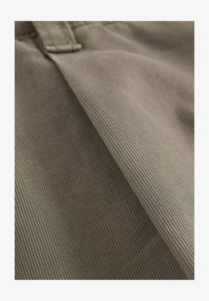 Brauner Baumwollstoff mit einer gerippten Textur, der zwei überlappende Abschnitte zeigt und ein sichtbares Verschlussdetail nahe der Oberseite aufweist.