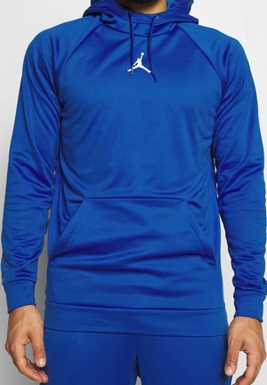Mężczyzna w niebieskiej bluzie z kapturem z białym logo Jumpman na piersi, z kieszenią kangura i kapturem ze sznurkiem.