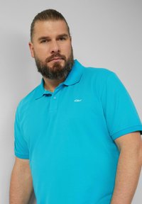 Türkise Polo-Shirt aus Baumwolle mit kurzen Ärmeln, Kragen und einer Knopfleiste mit zwei Knöpfen. Verfügt über ein kleines weißes Markenlogo auf der Brust.