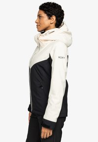 Roxy jacket met een two-tone ontwerp, zwart en crème kleuren, een capuchon, een rits aan de voorkant en gestructureerde mouwen. Inclusief zijzakken.
