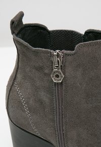 Stivale alla caviglia in suede grigio con cerniera laterale e dettaglio in metallo esagonale. Presenta una finitura leggermente testurizzata e un tacco nero robusto.