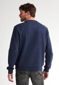 Dunkelblaues Sweatshirt mit gesprenkeltem Muster, Rundhalsausschnitt, gerippten Bündchen und Saum. Getragen mit grauen Denim-Jeans, von hinten betrachtet.