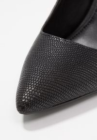 Černé lodičky s špičatou špičkou a povrchem s texturou hadí kůže a hladkým interiérem; elegantní design zdůrazňuje moderní styl.