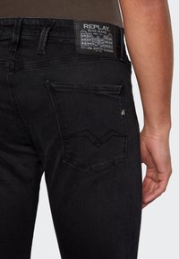 Černé džíny z denimu mají slim fit, viditelné švy a charakteristický design zadní kapsy. Štítek na pasu uvádí detaily o značce.