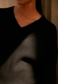 Pulover negru tricotat cu model în relief și decolteu în V, prezentând o suprafață texturată și o subtilă joacă de lumină și umbră pe întreaga țesătură.