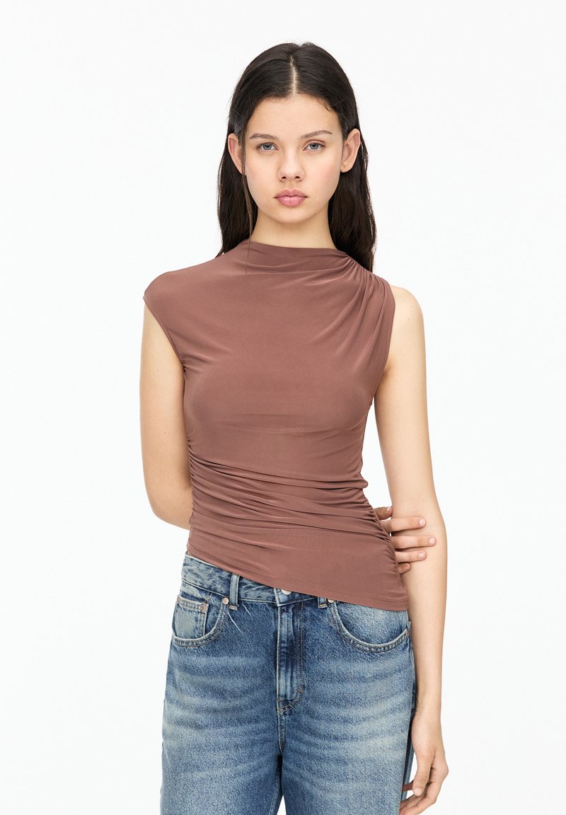Brown, fitted sleeveless top with asymmetrical neckline and gathered sides, paired with light blue high-waisted jeans. Smooth texture.