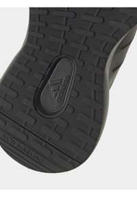 Svart gummisul med ett texturerat greppmönster, med horisontella och vertikala linjer, samt en präglad Adidas-logotyp. Non-marking design.