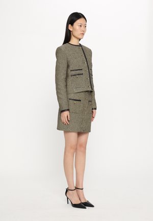 Veste en tweed au design court avec des finitions noires, associée à une mini-jupe en tweed assortie. Des chaussures à talons hauts noires complètent l'ensemble.