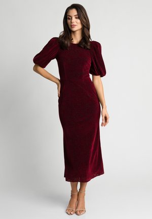 Bordowa sukienka midi z aksamitu z bufkami na rękawach, dopasowanym krojem, kwiatową fakturą i rozcięciem do kolana na dole. Proste beżowe szpilki.