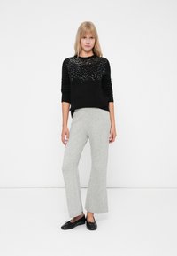 Maglione nero con scollatura rotonda, adornato con un motivo di perline nella parte superiore. Pantaloni in maglia a gamba svasata grigi. Scarpe nere senza lacci.