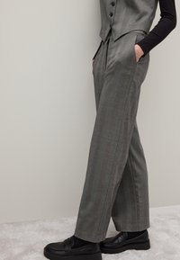 Pantaloni a quadri grigi realizzati in tessuto testurizzato, con vita alta, tasche frontali e design a gamba dritta. Indossati con mocassini neri.