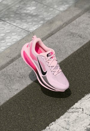 Zapatilla deportiva rosa con parte superior de malla, logo de swoosh negro y suela texturizada. Presenta un diseño ligero y una entresuela rosa llamativa.