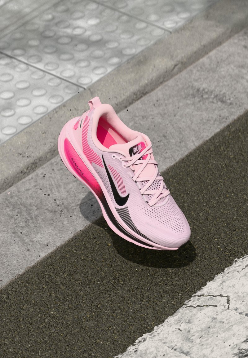 Basket économique rose avec tige en maille, logo swoosh noir et semelle texturée. Elle présente un design léger et une semelle intermédiaire rose audacieuse.