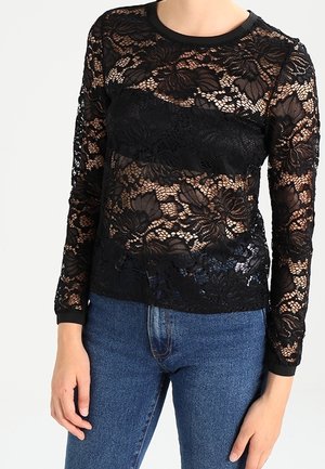 Haut en dentelle noire à manches longues avec des motifs floraux, un col rond et une texture transparente, associé à un jean bleu.