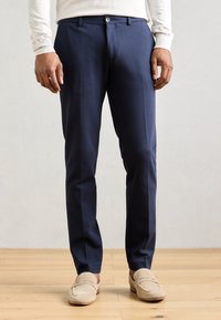Marineblauwe dresspants met een gladde textuur, een getailleerde pasvorm, een vlakke voorkant en twee zakken. In combinatie met beige instappers.