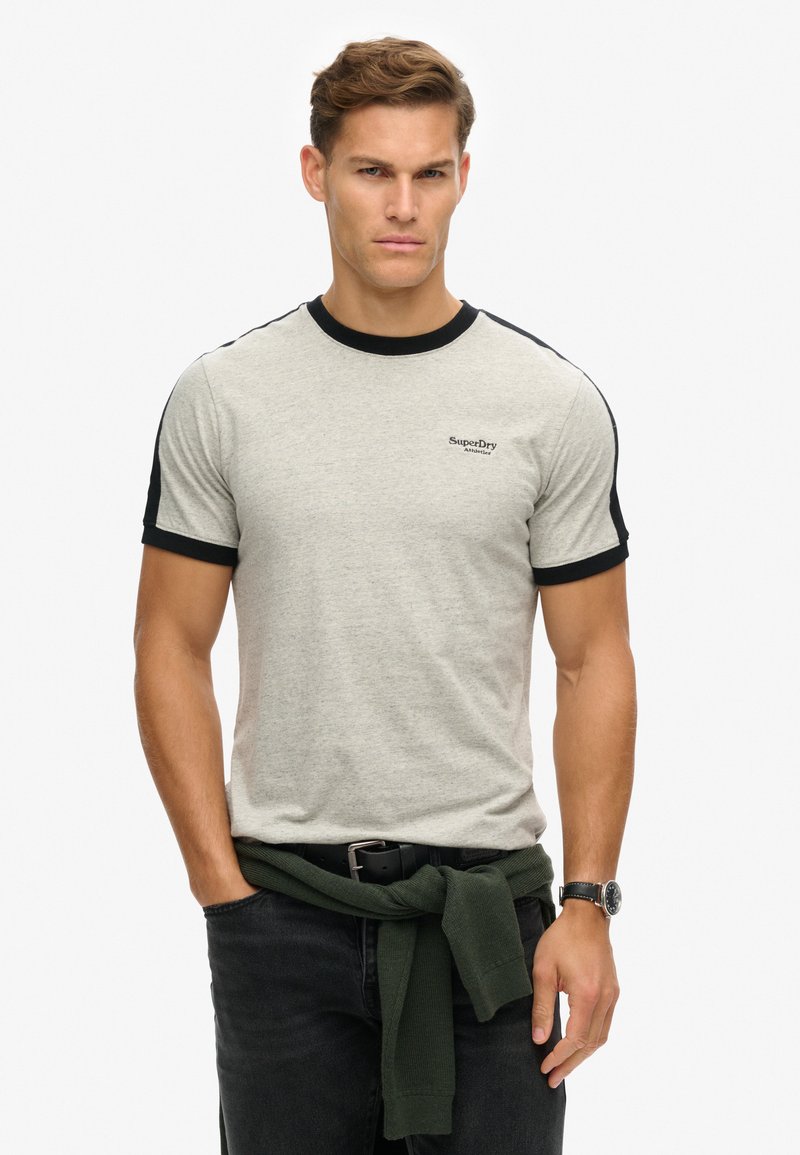 Grå T-shirt med korte ærmer og sorte detaljer på ærmerne og kraven. Har et lille "SuperDry" logo på brystet. Bæres med mørke jeans.