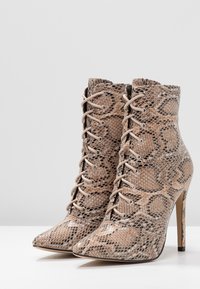 Snakeskin ankelstövlar med spetsig tå, beige och bruna mönster, snörning och en slank hög klack. Den texturerade ytan tillför detaljer.