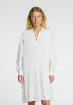 Hvid langærmet kjole med V-hals, der har fine broderier og udskæringer i kanten, lavet af let stof.