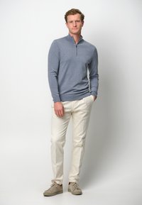 Himmelblauer Reißverschluss-Pullover mit langen Ärmeln, kombiniert mit cremefarbenen Hosen und beigen Turnschuhen. Einfaches Design mit einer taillierten Silhouette.