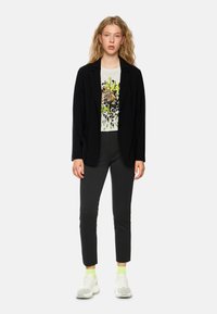 Black blazer over a graphic t-shirt featuring a leopard print, paired with slim-fit trousers and chunky white sneakers with neon accents.