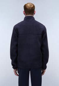 Marineblaue Fleecejacke mit hohem Kragen, strukturiertem Material und lockerer Passform. Sie hat lange Ärmel und eine horizontale Naht im Rücken.