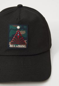 Svart baseballcap laget av stoff, med en rektangulær lapp med et geometrisk rødt og grønt design og ordet "BILLA BONG."