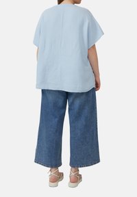 Lichtblauwe, gestructureerde top met korte mouwen, gecombineerd met wijde blauwe jeans en crèmewitte platform sandalen. Achteraanzicht; minimalistische stijl.