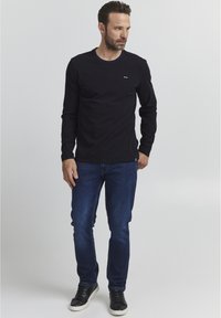 Sötétkék hosszú ujjú póló, ami pamutból készült, kerek nyakkivágással. Sötétkék farmernadrággal és fekete sportcipővel párosítva. Egyszerű dizájn, minimális részletezéssel.