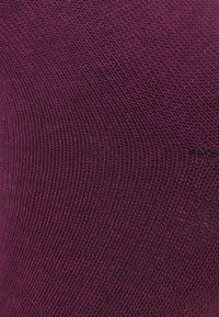 Tessuto testurizzato in un profondo bordeaux con un motivo a costine diagonali, che mette in mostra linee sottili e una superficie liscia e lavorata a maglia.