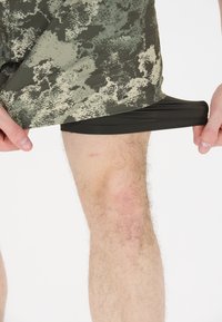 Shorts met een donker groen en licht beige camouflagepatroon, voorzien van een zwarte voering. De stof lijkt soepel en lichtgewicht.