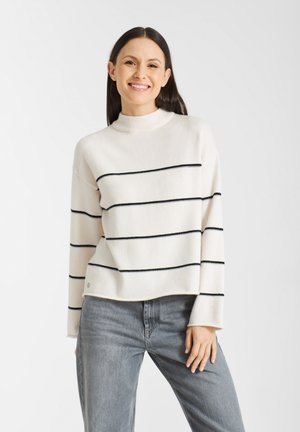 Creme turtleneck trui met zwarte horizontale strepen, losse pasvorm, zachte textuur en een cropped zoom. Gecombineerd met grijze jeans.