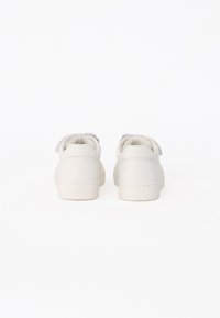 Une paire de baskets blanches avec des bandes velcro, vues de derrière sur un fond blanc.