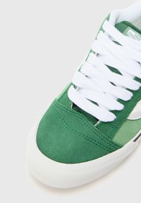 Green suede sneaker with white laces, featuring a smooth rubber sole and a contrasting side stripe design in light green.