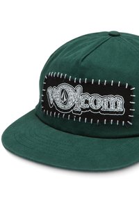 Cappello di tessuto verde con una toppa rettangolare nera cucita che mostra il logo "Volcom" in bianco. Presenta una visiera piatta e una superficie texturizzata.