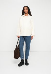 Crèmekleurig fleecetak met een halve rits, zijzakken, gecombineerd met blauwe spijkerbroek en zwarte chunky laarzen; houdt een bruine tas vast.