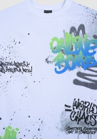 Biała koszulka z krótkim rękawem wykonana z bawełny, z kolorowym tekstem w stylu graffiti oraz plamami w zielonym, niebieskim i czarnym kolorze.